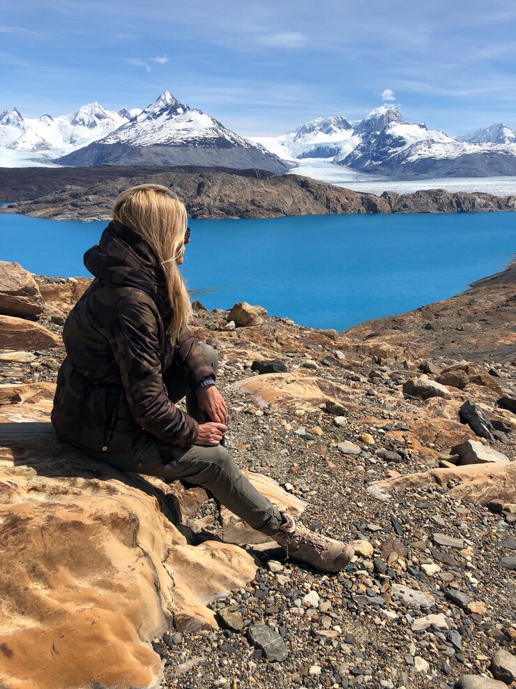 Photo woman looking away while sitting on rock against snowcapped mountains