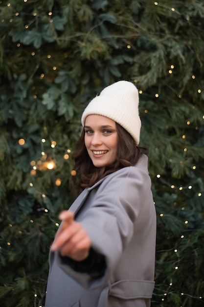 Donna che guarda la fotocamera sorridendo e tenendo il fuoco bengala vicino all'albero di natale concetto di vacanza atmosfera natalizia