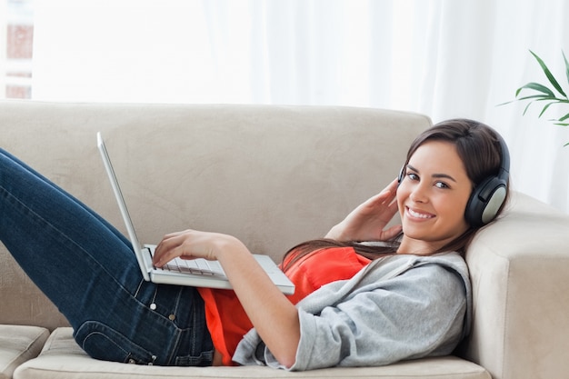 A woman looking at the camera while she uses a laptop and headphones