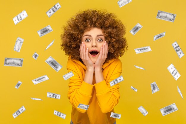 Woman looking at camera with big eyes absolutely shocked of\
money rain falling from up