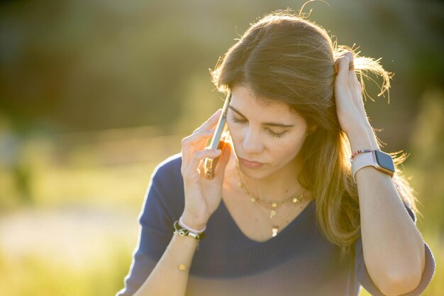 Foto donna che guarda in basso mentre parla al telefono all'aperto in natura in retroilluminazione concept tecnologico