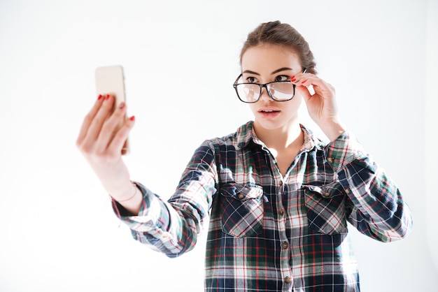 Женщина смотрит через очки и принимая селфи с мобильного телефона