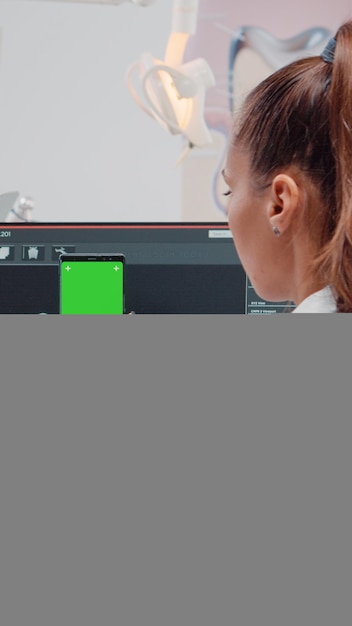 Photo woman looking at green screen on mobile phone for stomatological care at dentistry office. orthodontist holding smartphone with chroma key and mockup template on display for teethcare