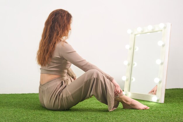 スタジオの床に座っている楽屋のために照らされた鏡で彼女の反射を見ている女性