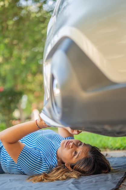 Женщина смотрит под свою машину, пытаясь выяснить, почему она не запускается.