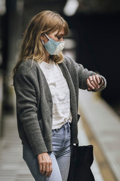 Donna che guarda l'orologio mentre aspetta il treno durante la pandemia di coronavirus