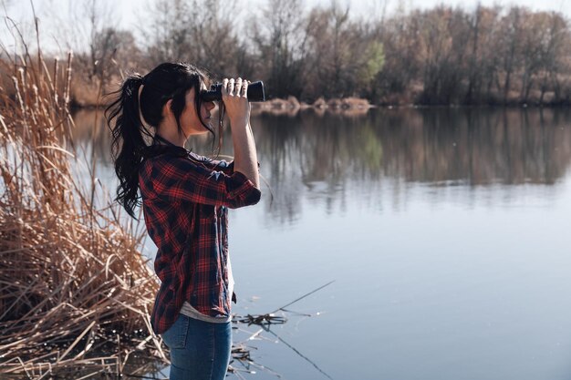 Photo woman looking at lake through binoculars