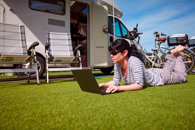 Женщина смотрит на ноутбук возле кемпинга. Отдых на караване. Семейный отдых, поездка на отдых в автодоме на колесах. Технология передачи информации о соединении Wi-Fi.