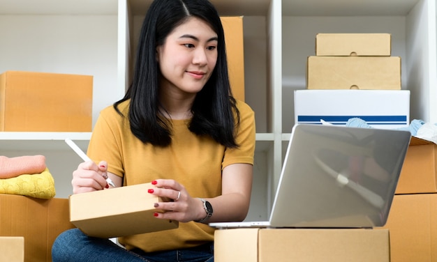woman looking at laptop screen and writing address on parcel box,online selling, parcel delivery.