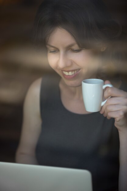 Donna che esamina un computer portatile con un caffè