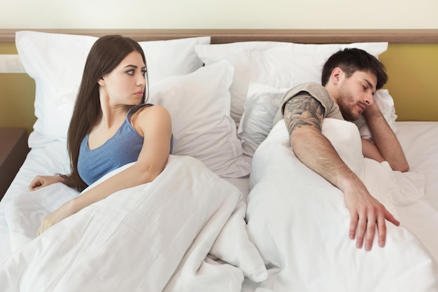 Woman looking at man while he sleeping in bed after quarrel