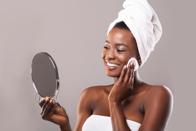 Woman looking in mirror and cleaning face with cotton pad