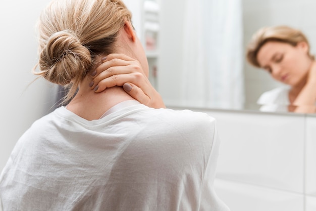 Foto donna che si guarda allo specchio con dolore al collo