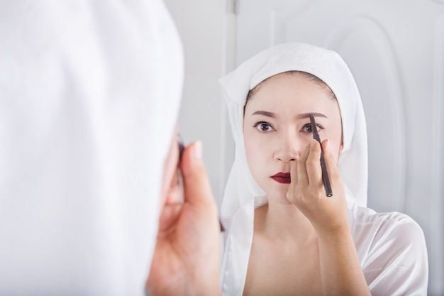 woman looking mirror and using pencil makeup eyebrow 