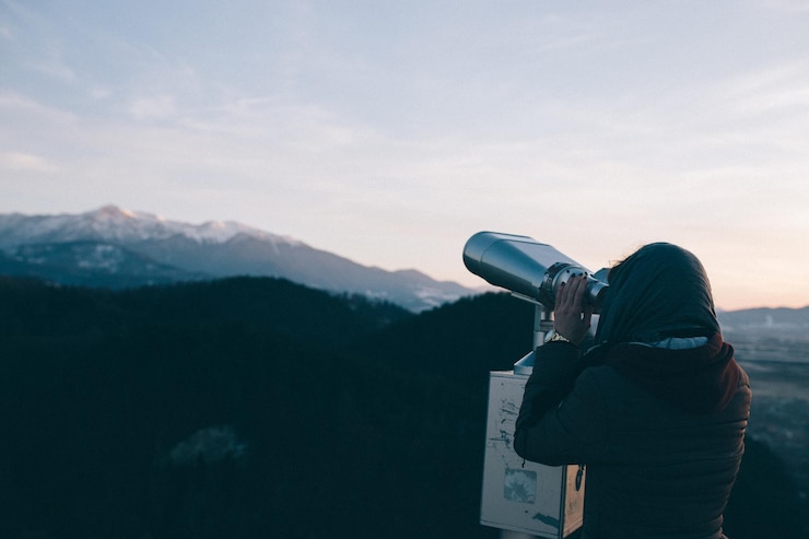 Photo woman looking at mountains through coin-operated binoculars against sky