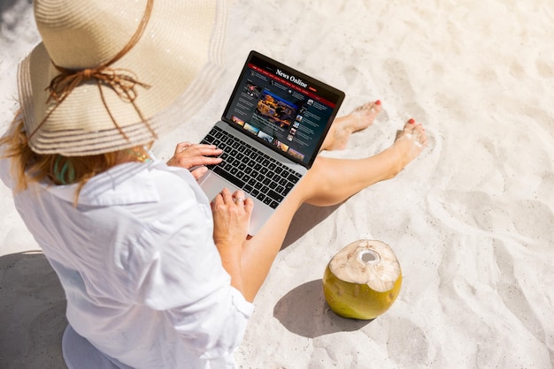 Женщина смотрит на новостной сайт на ноутбуке, сидя на пляже