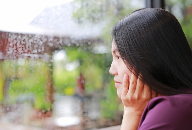 Woman looking out at glass window on rainy day