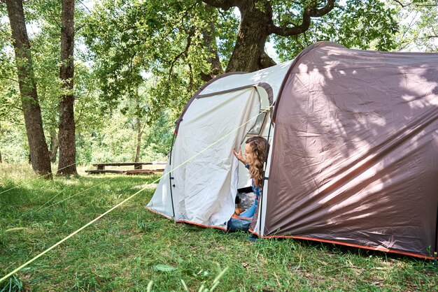 Donna che guarda fuori dalla tenda turistica sulla mattina di sole nella foresta