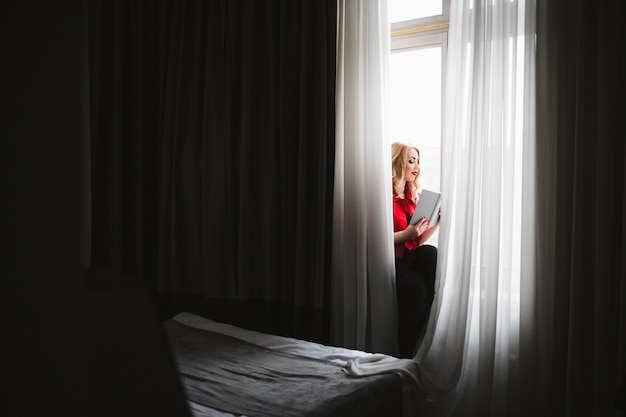 Woman looking out a window with white curtains