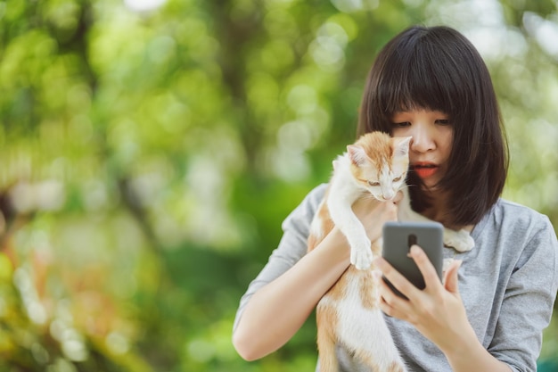 ぼやけた自然の背景を持つ猫と電話の画面を見ている女性