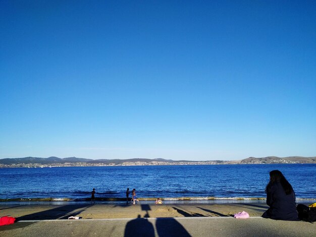 Woman looking at sea against clear blue sky