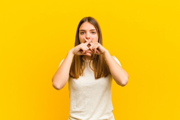 woman looking serious and displeased with both fingers crossed up front in rejection, asking for silence