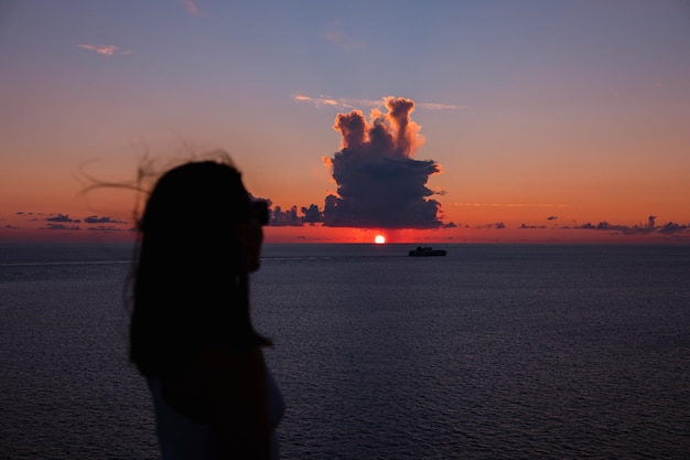 バックグラウンドで海の船の上の夕日を見ている女性