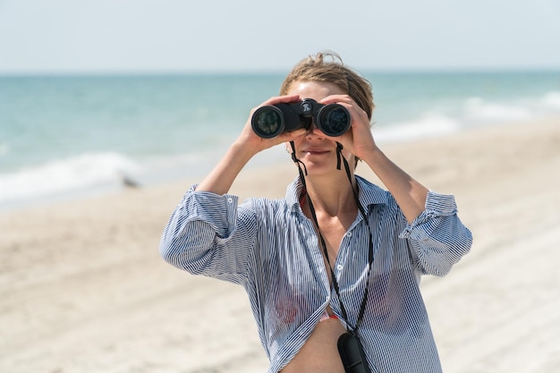 Foto donna che guarda tramite il binocolo su una spiaggia del mare. concetto di turismo della natura selvaggia