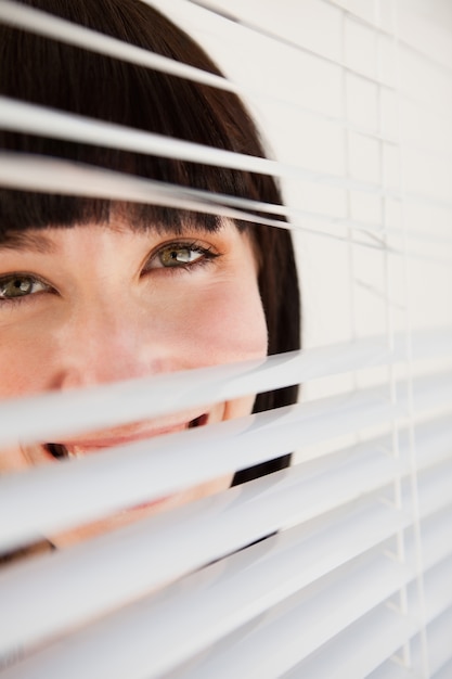 A woman looking through blinds she has opened slightly