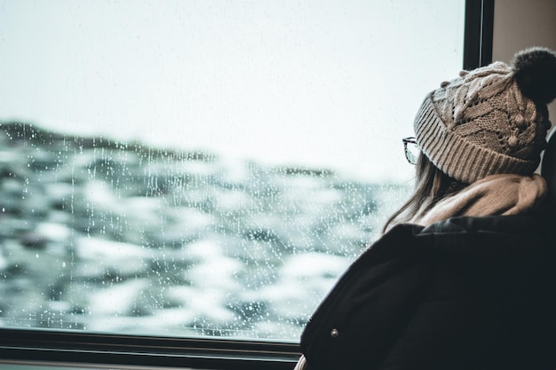 Photo woman looking through window during winter