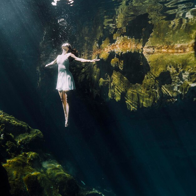 Foto donna che guarda in alto sotto l'acqua da una formazione rocciosa