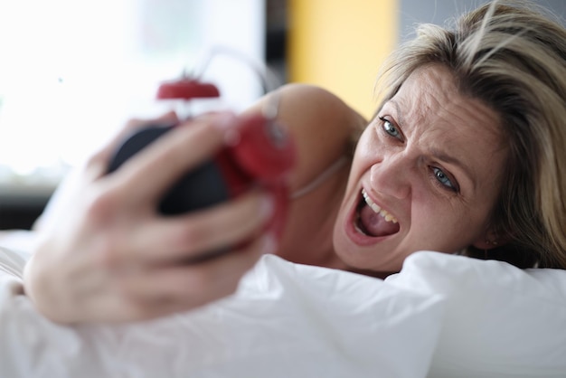 Woman looks at alarm clock and yells to bed