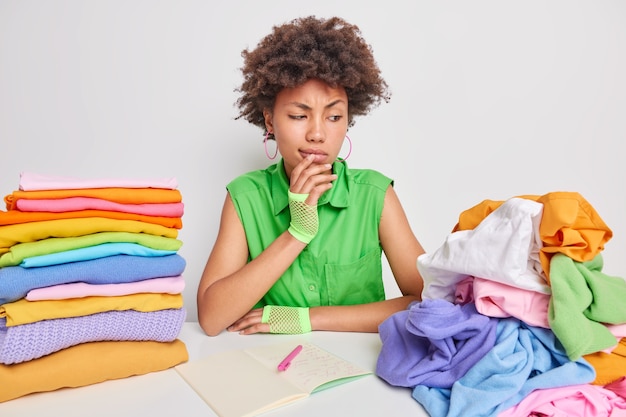 женщина внимательно смотрит на развернутую кучу белья, занятую складыванием одежды, делает заметки в блокноте, сидит возле стола, изолированного на белом