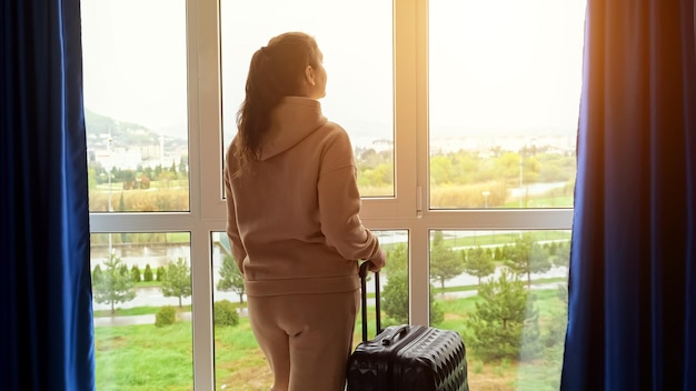 Женщина смотрит на городской пейзаж за окном и готовится к поездке