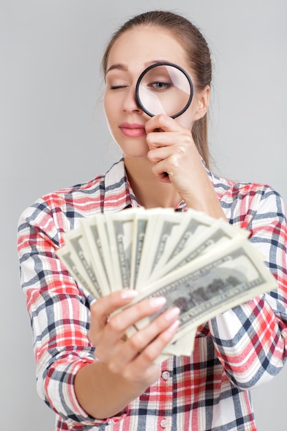 Woman looks in magnifier on dollar bills