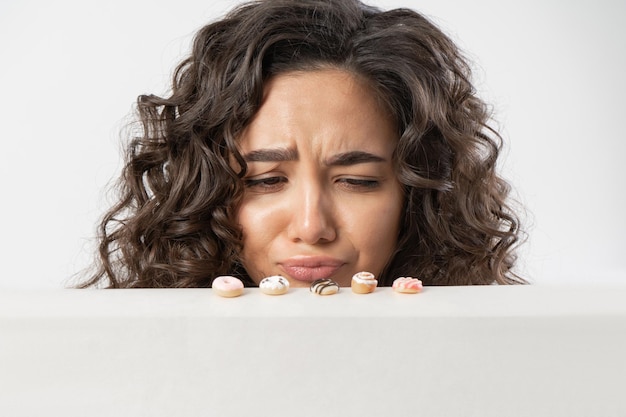 A woman looks at miniature sweet donuts with disappointment and resentment