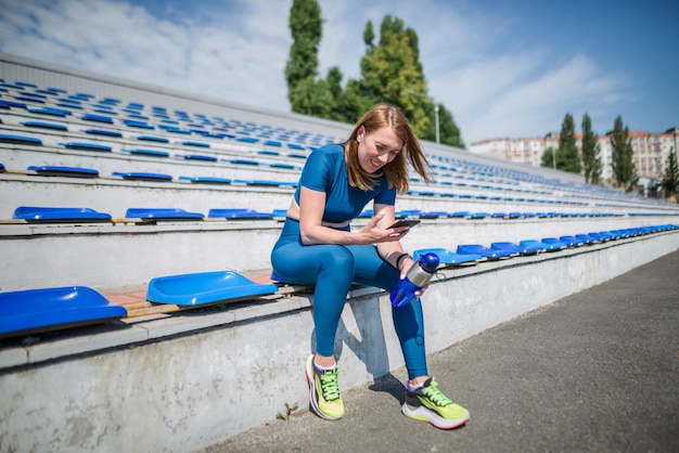 A woman looks at the phone while sitting on the podium of the stadium Healthy lifestyle