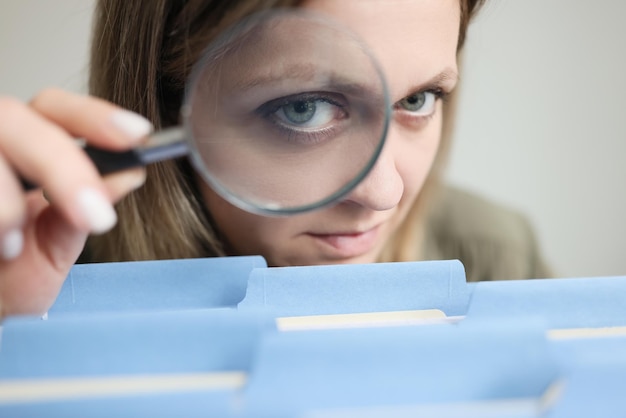 Photo woman looks through magnifier glass on blue folders with files put in row secretary looks for