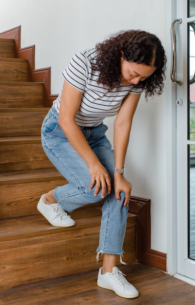 Woman loses control and cannot walk on stairs, she stops and hold her knees for support and rest with feel tingling. Concept of Guillain barre syndrome and numb legs disease or vaccine side effect.