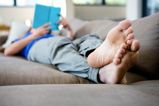 woman lying barefoot on the couch reading a book