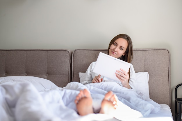 Woman lying in bed under blanket with tablet