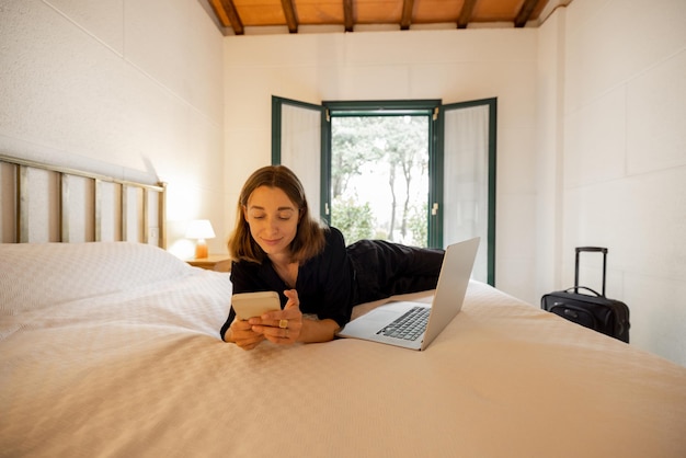 Woman lying on bed and using gadgets in hotel room