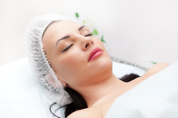 Woman lying on bed while getting beauty injection in neck. Facial treatments. Beauty concept.