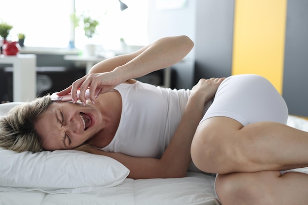 Foto donna sdraiata a letto con lo stomaco malato e urlando nel telefono cellulare