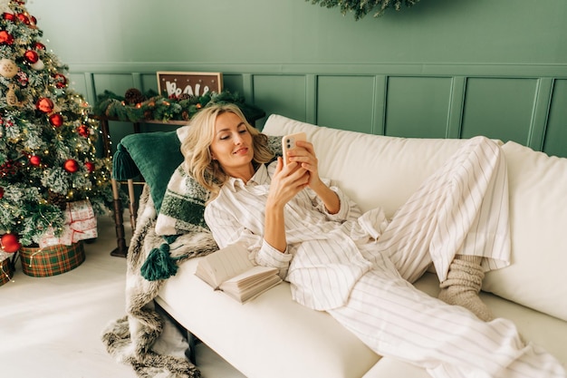 クリスマスにソファに横たわっている女性が携帯電話を使っている