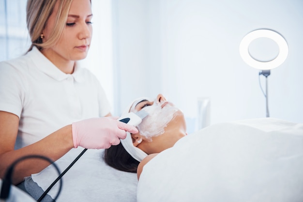 Woman lying down in spa salon and have face cleaning procedure by professional cosmetologist.