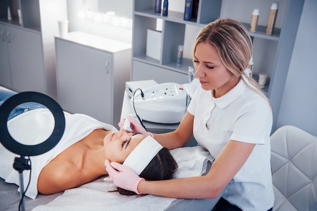 Woman lying down in spa salon and have face cleaning procedure by professional cosmetologist.