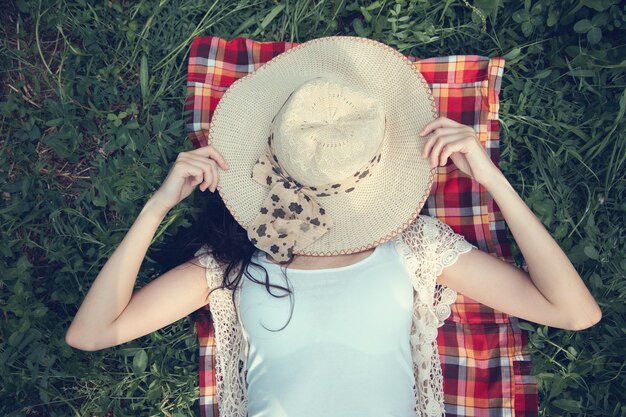 Foto donna sdraiata sul cappello di erba sul viso