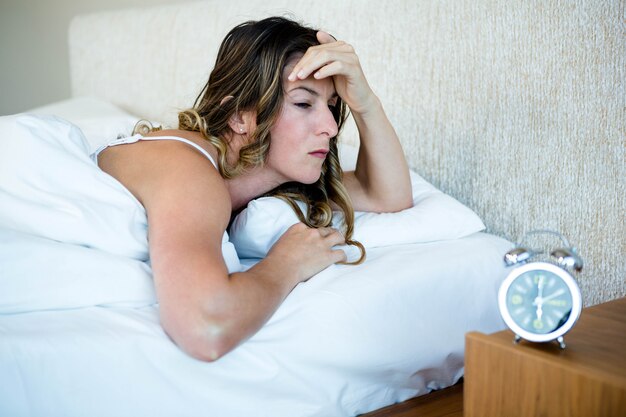 Woman lying in her bed looking stressed, next to an alarm clock