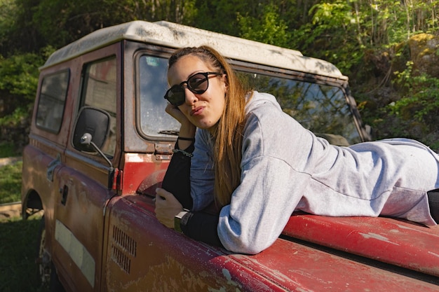 Woman lying on the hood of an old red offroad vehicle pensive